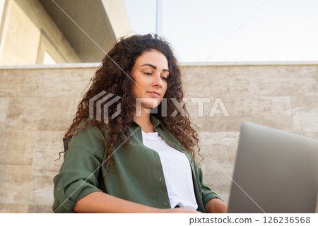 Young curly girl works at laptop sitting, work online, shopping online, communication in social networks, online learning, freelancer 126236568