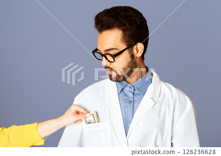 Corruption in medicine. Female patient putting money into Indian doctor's pocket on lilac background 126236628