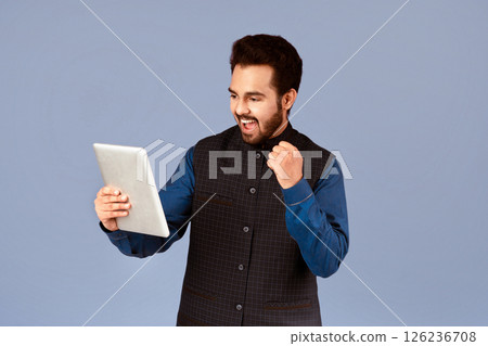 Excited Indian man with tablet computer making YES gesture on violet background Excited Indian man with tablet computer making YES gesture on violet background 126236708