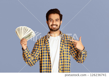 Smiling Indian man pointing at fan of money over lilac background, copy space Smiling Indian man pointing at fan of money over lilac background, copy space 126236741