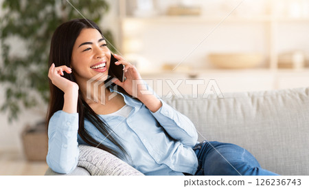 Phone Talk. Joyful asian girl talking on cellphone at home, relaxing on couch in living room, copy space Phone Talk. Joyful asian girl talking on cellphone at home, relaxing on couch in living room, copy space 126236743