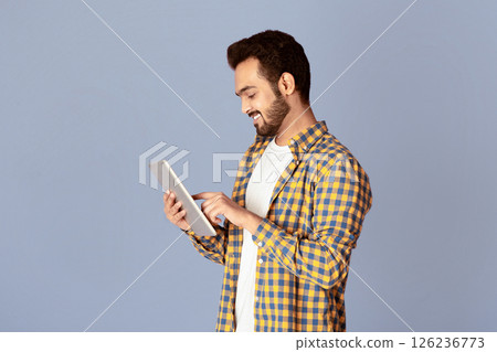Handsome Indian guy using tablet computer for online work or communication on violet background, panorama Handsome Indian guy using tablet computer for online work or communication on violet background, panorama 126236773