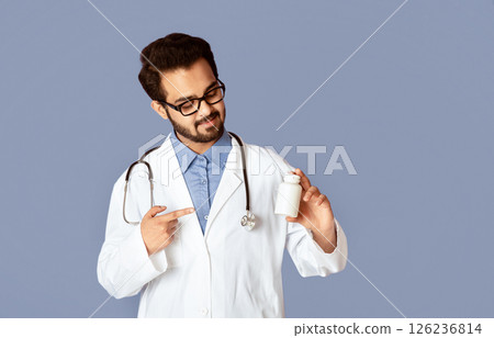 Confident Indian doctor pointing at jar of pills over lilac background, mockup for design Confident Indian doctor pointing at jar of pills over lilac background, mockup for design 126236814