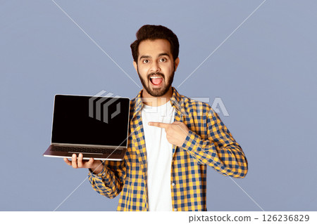 Excited Indian guy pointing at empty laptop screen over violet background, mockup for website design. Panorama 126236829