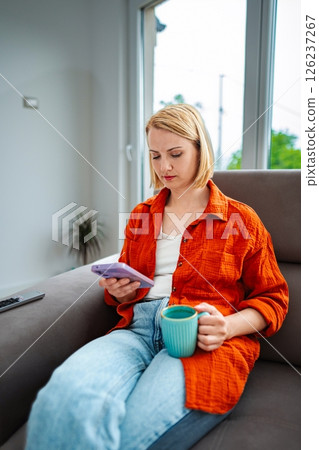 Young woman relaxing on a couch with a drink and phone Young woman relaxing on a couch with a drink and phone 126237267
