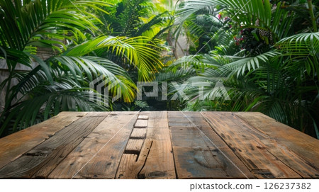 A wooden tabletop sits in front of a lush, tropical garden with palm trees and green foliage. 126237382