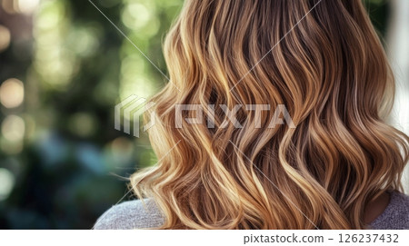 Long, wavy blonde hair cascades down the back of a person, illuminated by soft sunlight in a lush garden. 126237432