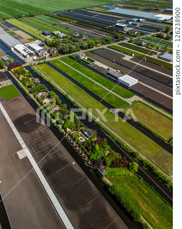 Aerial view of a lush countryside garden surrounded by canals and farmlands, with a cozy house and colorful trees, set in a peaceful rural landscape under a clear blue sky. 126238900