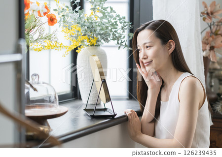 Smiling woman checking her skin in the mirror 126239435
