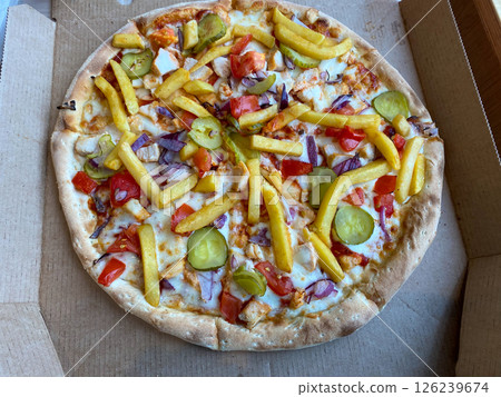 A hearty pizza with veggies, meat and fries rests on a paper box 126239674