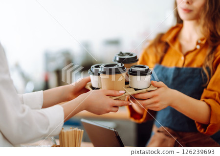 Young woman owner of a coffee shop behind the bar prepares coffee. Concept of orders to go. Young woman owner of a coffee shop behind the bar prepares coffee. Concept of orders to go. 126239693