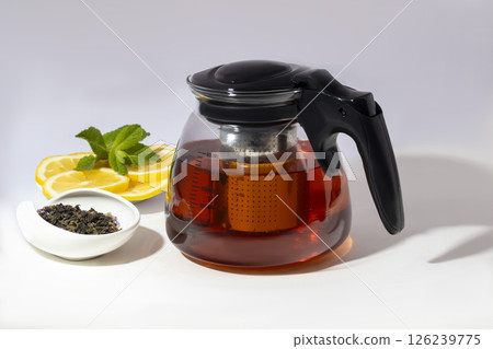 Glass teapot with metal strainer inside. Kitchen utensils on gray background. Glass teapot with metal strainer inside. Kitchen utensils on gray background. 126239775