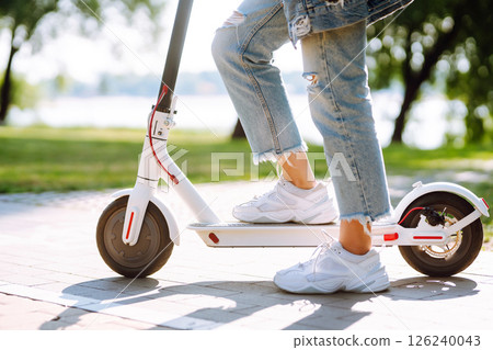 Woman riding electric kick scooter outdoors at sunset, closeup. Ecological transportation concept. 126240043