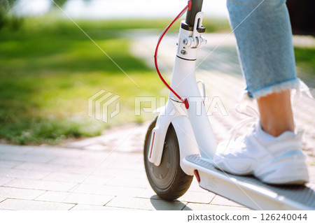 Woman riding electric kick scooter outdoors at sunset, closeup. Ecological transportation concept. 126240044