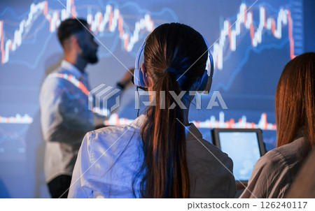 View from behind the woman. Male leader talking to employees, showing the plan on the projector in office View from behind the woman. Male leader talking to employees, showing the plan on the projector in office 126240117