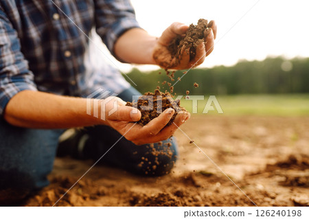 Soil is in the strong hands of a farmer on a black field. Agriculture or gardening concept. 126240198
