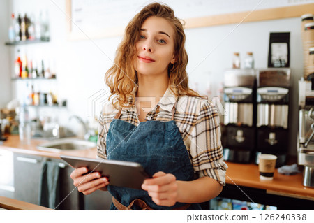 Successful small business owner stands behind counter of coffee shop with digital tablet takes order Successful small business owner stands behind counter of coffee shop with digital tablet takes order 126240338