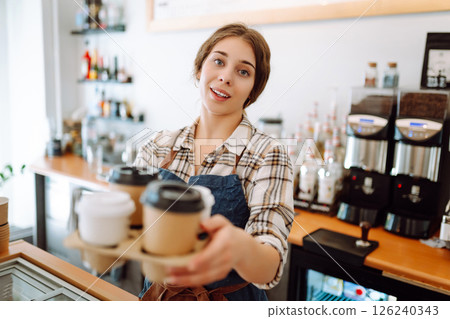 Portrait of a young female barista with a glass holder with drinks to go. Takeaway delivery concept. Portrait of a young female barista with a glass holder with drinks to go. Takeaway delivery concept. 126240343