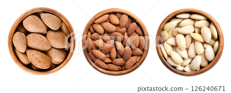 Almonds in shell, shelled and skinless, in wooden bowls. On the left side unshelled almonds, in the center with their shell removed, but still with brown seed coats, and blanched on the right side. 126240671
