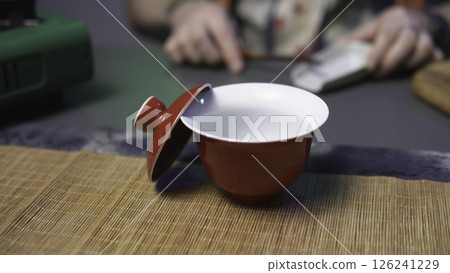 An Artistic Red Tea Cup with a Lid Sits on a Warm Wooden Surface Evoking Calm and Serenity. Media An Artistic Red Tea Cup with a Lid Sits on a Warm Wooden Surface Evoking Calm and Serenity. Media 126241229