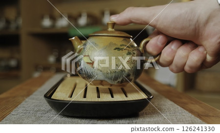 A person pours tea into a teapot on a wooden table, creating tranquility. Media A person pours tea into a teapot on a wooden table, creating tranquility. Media 126241330
