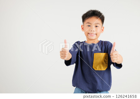 Confident Asian young boy in a studio portrait isolated on white background makes a thumbs up OK sign, symbolizing agreement and success. primary child smile radiates positivity and satisfaction 126241658