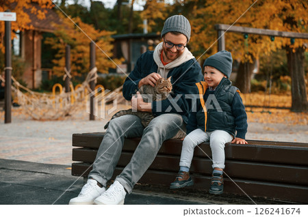 Sitting with cute cat. Father and young son is together outdoors at daytime Sitting with cute cat. Father and young son is together outdoors at daytime 126241674