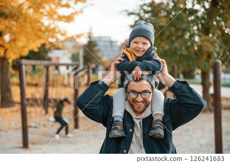 Holding boy on the shoulders. Father and young son is together outdoors at daytime Holding boy on the shoulders. Father and young son is together outdoors at daytime 126241683