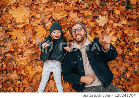 Laying down on the ground that covered with fallen leaves. Father and young son is together outdoors at daytime 126241704