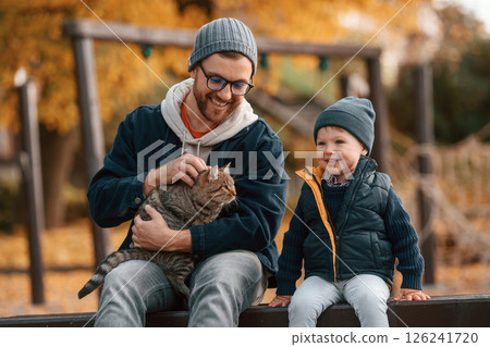 Petting a cat. Father and young son is together outdoors at daytime 126241720