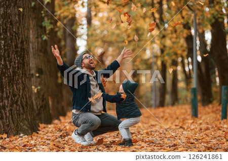 Playing with fallen leaves. Father and young son is together outdoors at daytime 126241861