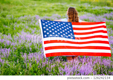 Young woman proudly hold waving american USA flag on blooming meadow. 4th of July. Independence Day. 126242134