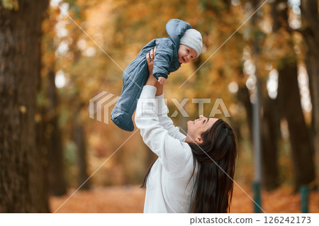Beautiful mother holding her little son in hands. Standing in the autumn forest Beautiful mother holding her little son in hands. Standing in the autumn forest 126242173