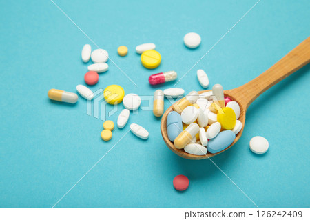 Assorted pharmaceutical medicine pills, tablets and capsules on wooden spoon on blue background. 126242409