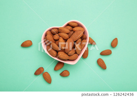 Fresh natural healthy almonds nuts in heart shaped bowl on mint background. 126242436