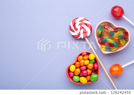 Different types of candies on purple background, copy space. Colorful birthday party background. Top view Different types of candies on purple background, copy space. Colorful birthday party background. Top view 126242450