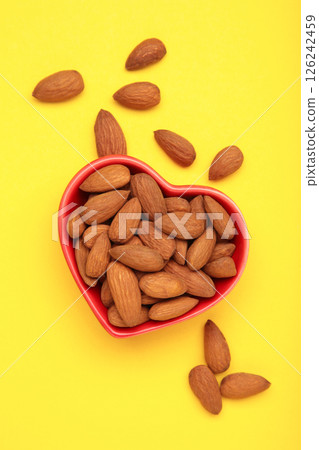 Fresh natural healthy almonds nuts in heart shaped bowl on yellow background. Vertical photo. Fresh natural healthy almonds nuts in heart shaped bowl on yellow background. Vertical photo. 126242459