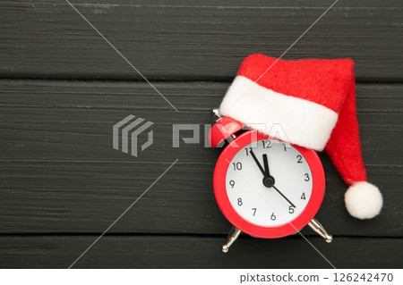 Red alarm clock with Christmas Santa hat on black wooden background. Top view. 126242470