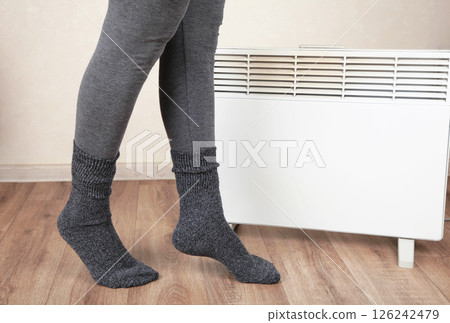 Young woman in warm socks near electric heater at home. Concept of heating season. Top view 126242479