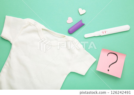 The pregnancy test with two stripes and baby cloth on mint background. Health care concept. Top view 126242491