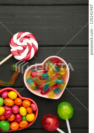 Different types of candies on black wooden background, copy space. Colorful birthday party background. Vertical photo Different types of candies on black wooden background, copy space. Colorful birthday party background. Vertical photo 126242497