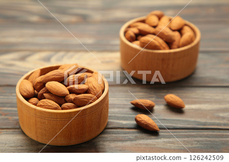 Fresh natural healthy almonds nuts in two wooden bowl on brown wooden background. 126242509