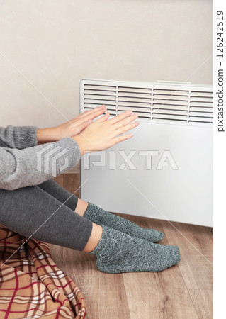 Young woman in warm socks near electric heater at home. Concept of heating season. Top view 126242519
