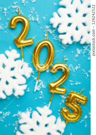 Holiday background Happy New Year 2025. Numbers of year 2025 made by gold candles with snowflakes on blue background. 126242522