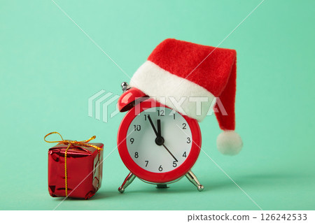 Red alarm clock with Christmas Santa hat on mint background. Top view. Red alarm clock with Christmas Santa hat on mint background. Top view. 126242533