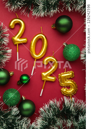 Merry Christmas and Happy New Year 2025. Golden candles numbers 2025 with green balls on red background. Top view Merry Christmas and Happy New Year 2025. Golden candles numbers 2025 with green balls on red background. Top view 126242596