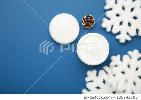 Cold protecting winter cream concept. Jar cosmetics with snowflakes on blue background. Winter seasonal skin care Cold protecting winter cream concept. Jar cosmetics with snowflakes on blue background. Winter seasonal skin care 126242598