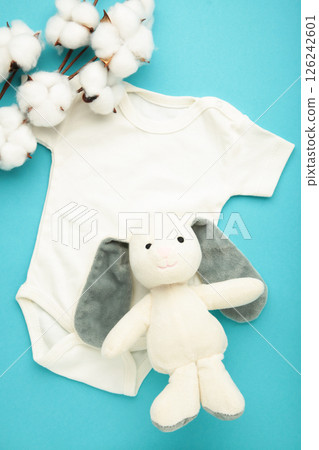 White baby short sleeve bodysuit with soft toy bunny and cotton flower on blue. Top view White baby short sleeve bodysuit with soft toy bunny and cotton flower on blue. Top view 126242601