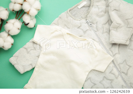 White baby short sleeve bodysuit with cotton flower on mint background. Top view 126242639