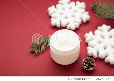 Cold protecting winter cream concept. Jar cosmetics with snowflakes and fir tree branches on red background. Winter seasonal skin care Cold protecting winter cream concept. Jar cosmetics with snowflakes and fir tree branches on red background. Winter seasonal skin care 126242768